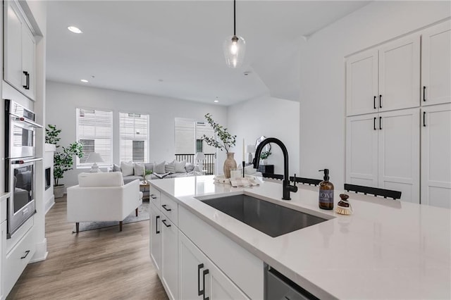 kitchen with light wood-type flooring, stainless steel double oven, sink, white cabinets, and hanging light fixtures