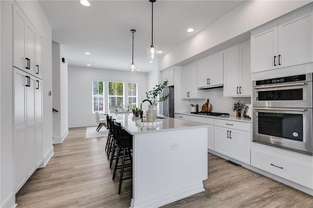 kitchen with appliances with stainless steel finishes, pendant lighting, white cabinets, a breakfast bar area, and an island with sink