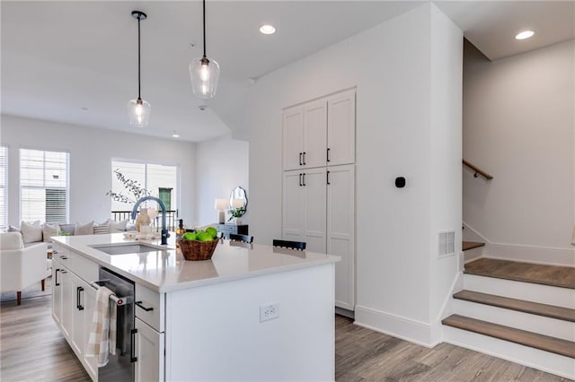 kitchen with white cabinetry, dishwasher, sink, hanging light fixtures, and an island with sink