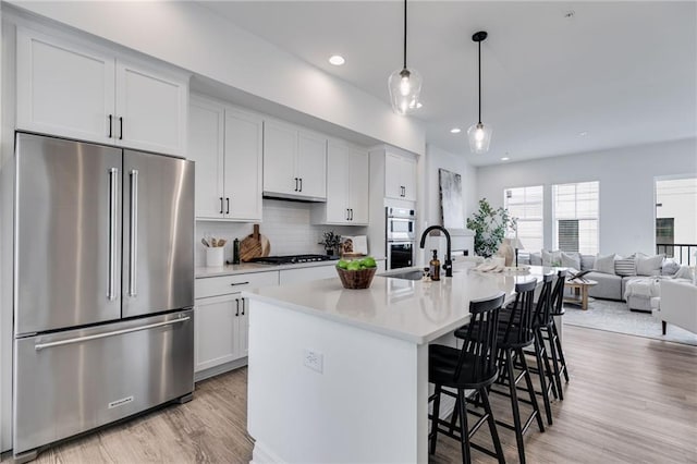 kitchen with stainless steel appliances, an island with sink, decorative light fixtures, decorative backsplash, and white cabinets