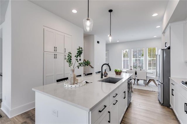 kitchen featuring stainless steel appliances, sink, white cabinetry, hanging light fixtures, and an island with sink