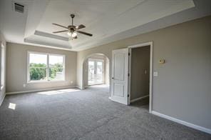 empty room with ceiling fan, a raised ceiling, and dark colored carpet