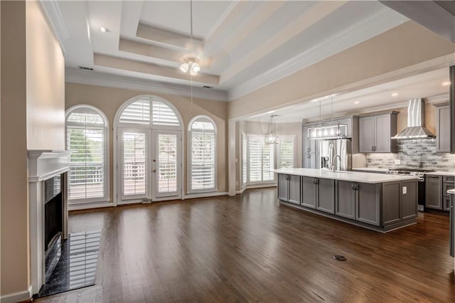 kitchen featuring gray cabinetry, light countertops, a tray ceiling, stainless steel appliances, and wall chimney exhaust hood