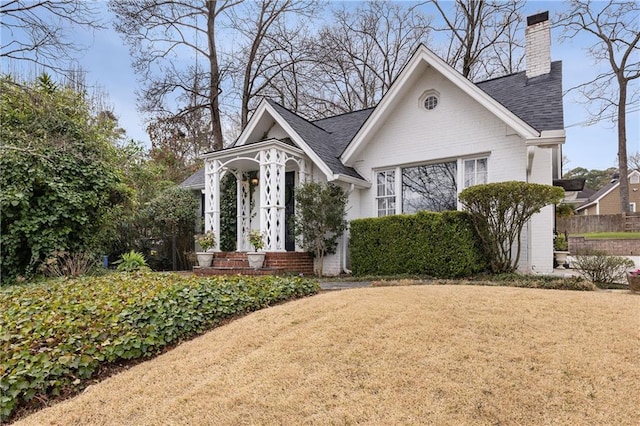 view of front of home with brick siding, a chimney, a front yard, and a shingled roof