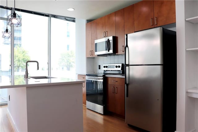 kitchen with sink, light hardwood / wood-style flooring, appliances with stainless steel finishes, hanging light fixtures, and tasteful backsplash