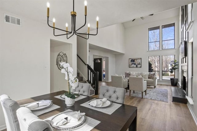 dining area with a notable chandelier, wood finished floors, a towering ceiling, visible vents, and stairway