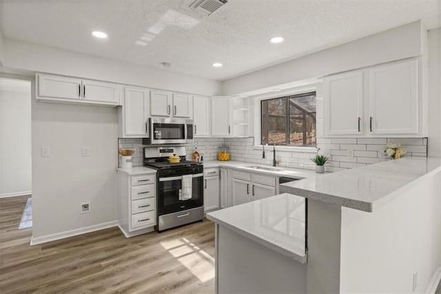 kitchen featuring stainless steel appliances, a peninsula, a sink, white cabinetry, and open shelves