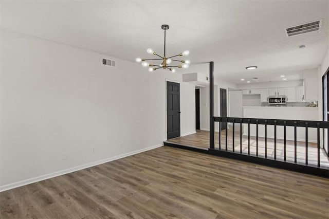 empty room featuring an inviting chandelier, baseboards, visible vents, and wood finished floors