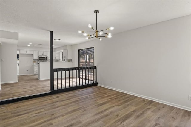 empty room featuring light wood-style flooring, baseboards, and a notable chandelier