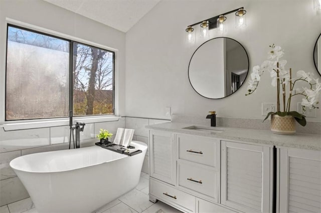 bathroom featuring marble finish floor, a wainscoted wall, a soaking tub, vaulted ceiling, and vanity