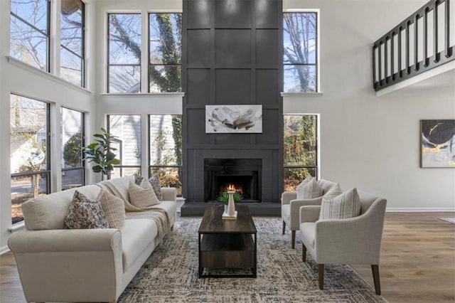 living room featuring baseboards, a fireplace, a high ceiling, and wood finished floors