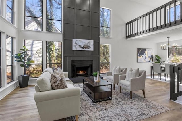 living area featuring a chandelier, a large fireplace, a high ceiling, baseboards, and light wood-style floors