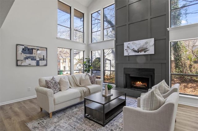 living area with high vaulted ceiling, a large fireplace, baseboards, and wood finished floors