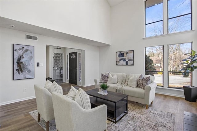 living room with a high ceiling, visible vents, baseboards, and wood finished floors