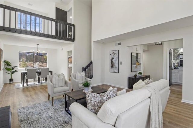 living room featuring baseboards, visible vents, wood finished floors, stairs, and a notable chandelier