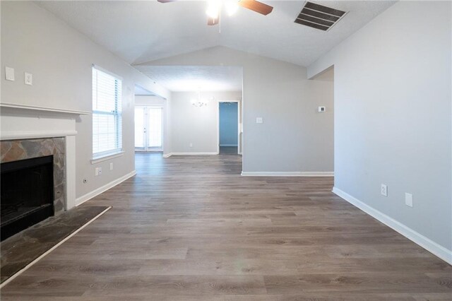 unfurnished living room featuring hardwood / wood-style flooring, lofted ceiling, a stone fireplace, and ceiling fan with notable chandelier