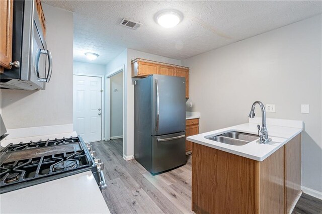 kitchen featuring sink, light hardwood / wood-style flooring, stainless steel appliances, a textured ceiling, and kitchen peninsula