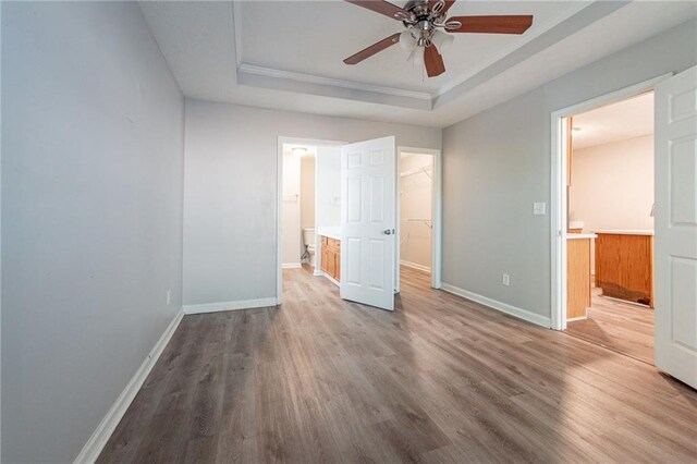 unfurnished bedroom with hardwood / wood-style flooring, a walk in closet, connected bathroom, and a tray ceiling