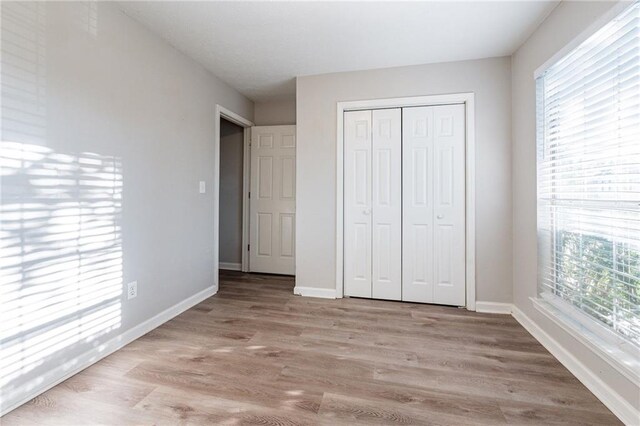 unfurnished bedroom with multiple windows, light wood-type flooring, and a closet