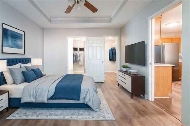 bedroom featuring stainless steel refrigerator, a spacious closet, a raised ceiling, and light hardwood / wood-style floors