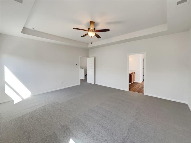 unfurnished room with dark colored carpet, baseboards, a raised ceiling, and ceiling fan