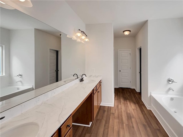 full bath featuring double vanity, a bath, wood finished floors, and a sink