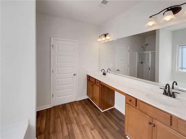 bathroom featuring wood finished floors, visible vents, double vanity, a stall shower, and a sink