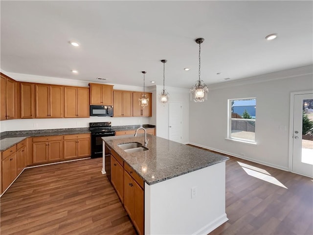 kitchen featuring dark wood finished floors, dark stone countertops, black appliances, and a sink