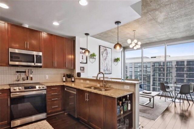 kitchen with stainless steel appliances, dark wood-type flooring, a sink, a peninsula, and decorative backsplash