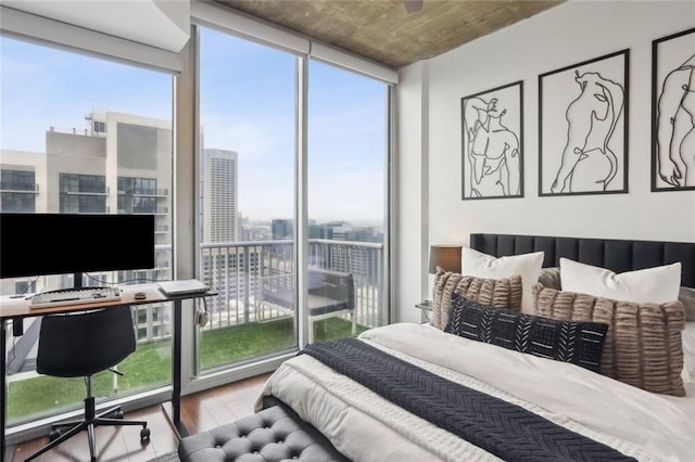 bedroom featuring wood finished floors, a wall of windows, an office area, and access to outside