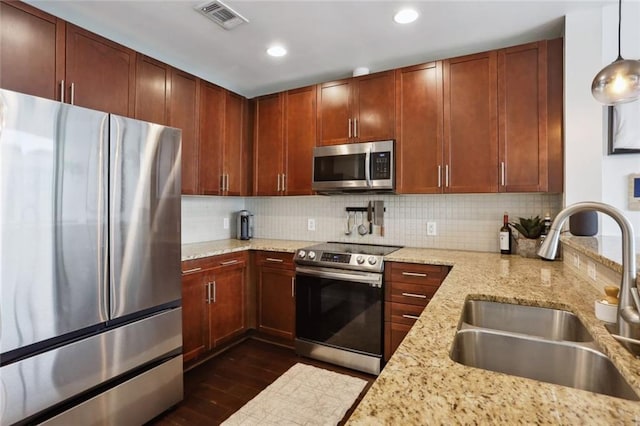 kitchen featuring appliances with stainless steel finishes, a sink, dark wood-style flooring, light stone counters, and backsplash