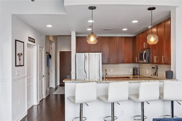 kitchen with stainless steel appliances, a peninsula, light stone countertops, backsplash, and dark wood-style flooring