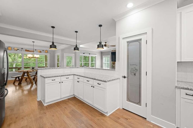 kitchen featuring white cabinetry, light stone countertops, backsplash, hanging light fixtures, and light wood-type flooring