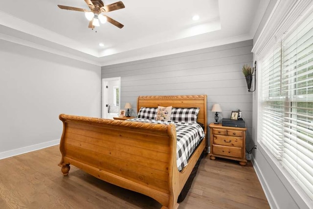 bedroom featuring wood walls, a tray ceiling, hardwood / wood-style flooring, and ceiling fan