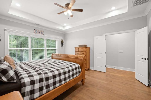 bedroom with a tray ceiling, crown molding, ceiling fan, and light hardwood / wood-style flooring