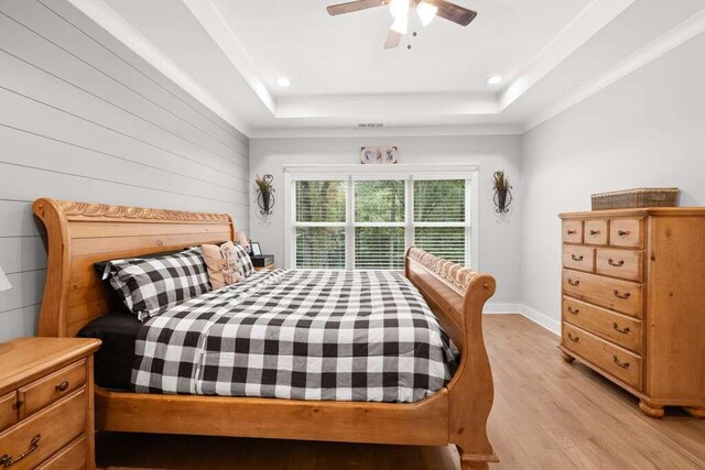 bedroom featuring ceiling fan, light wood-type flooring, and a tray ceiling