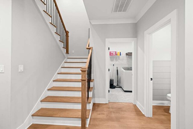 stairway featuring washing machine and clothes dryer, hardwood / wood-style flooring, and ornamental molding