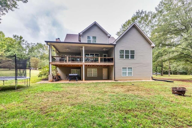 back of house featuring a lawn, an outdoor fire pit, a trampoline, and a patio area