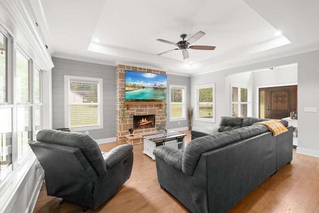 living room with ceiling fan, a fireplace, a raised ceiling, wooden walls, and light wood-type flooring