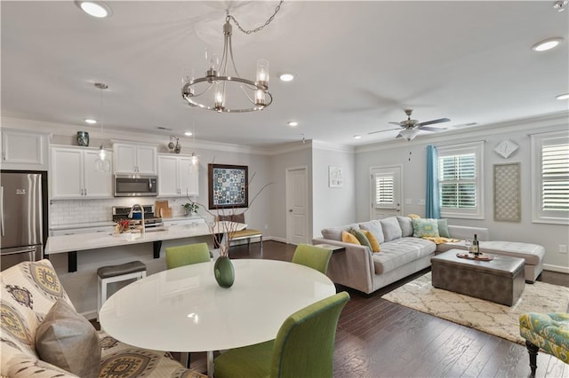 dining room with crown molding, dark wood-type flooring, sink, and ceiling fan with notable chandelier