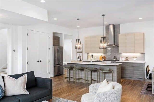 kitchen with modern cabinets, wall chimney range hood, high quality fridge, light countertops, and tasteful backsplash