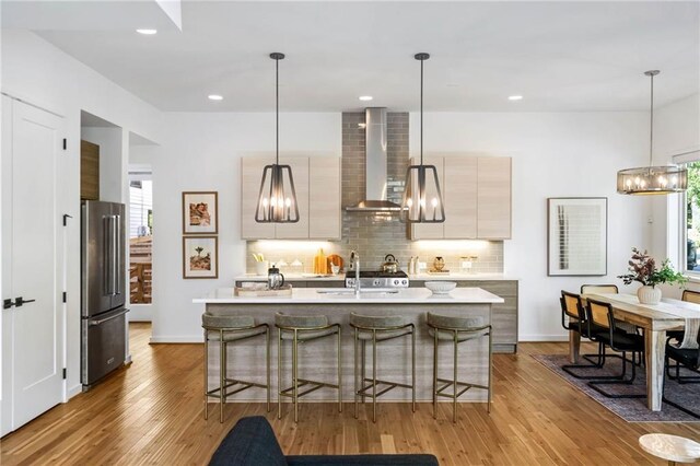kitchen with high end fridge, an inviting chandelier, light countertops, wall chimney exhaust hood, and tasteful backsplash