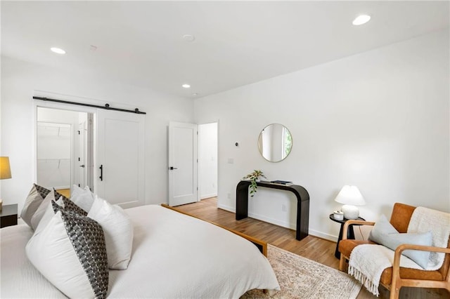 bedroom with a barn door, recessed lighting, and wood finished floors