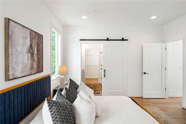 bedroom featuring recessed lighting, a barn door, and light wood-type flooring