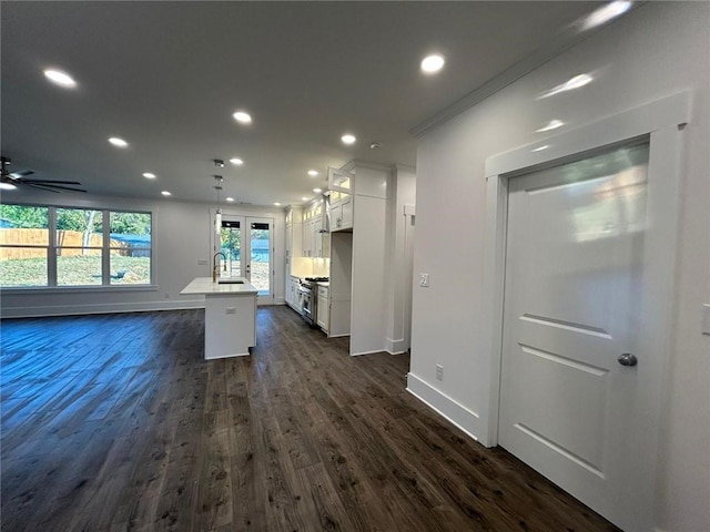 kitchen featuring dark hardwood / wood-style floors, stainless steel range, a center island with sink, decorative light fixtures, and white cabinets