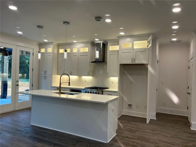 kitchen with white cabinets, hanging light fixtures, a kitchen island with sink, wall chimney exhaust hood, and sink