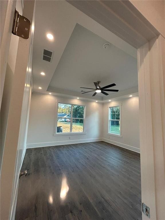 empty room featuring dark wood-type flooring, ceiling fan, a tray ceiling, and a wealth of natural light