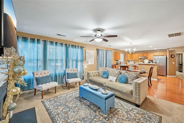 living area featuring ceiling fan with notable chandelier, visible vents, and light carpet