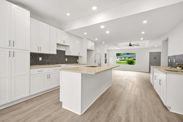 kitchen featuring a sink, decorative backsplash, light wood finished floors, and white cabinetry