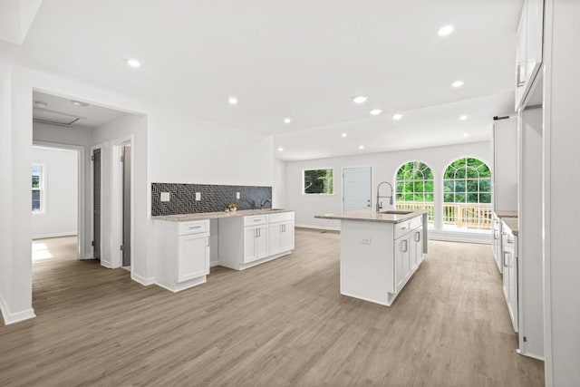 kitchen with white cabinets, a center island with sink, a sink, and light wood-style floors